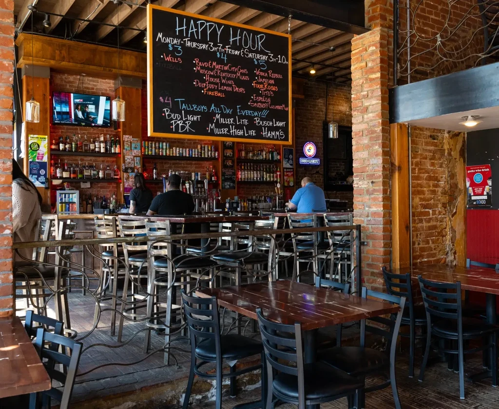 Rustic bar interior with a 'HAPPY HOUR' sign and liquor bottles.