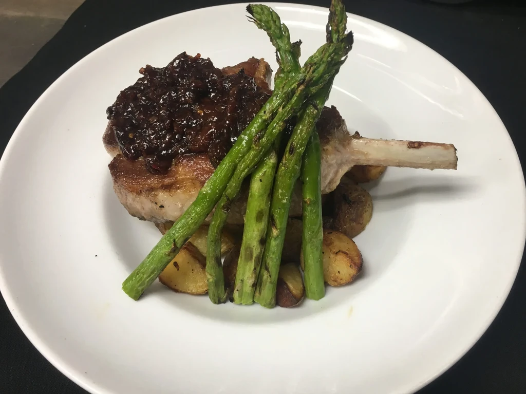 Bone-in pork chop with dark sauce, asparagus, and roasted potatoes.