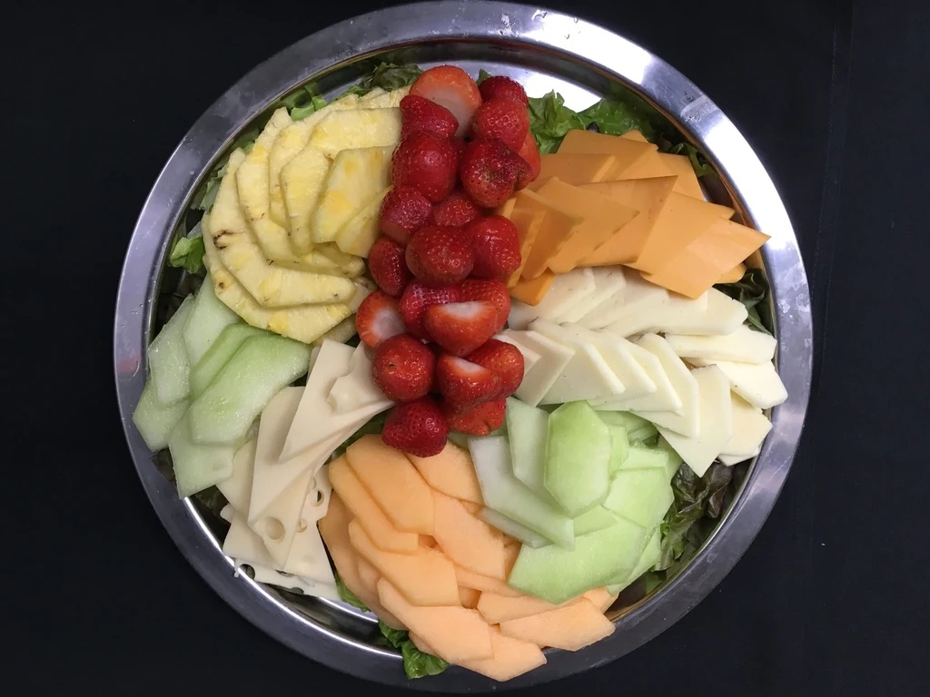Colorful fruit and cheese platter on a silver dish with greens.