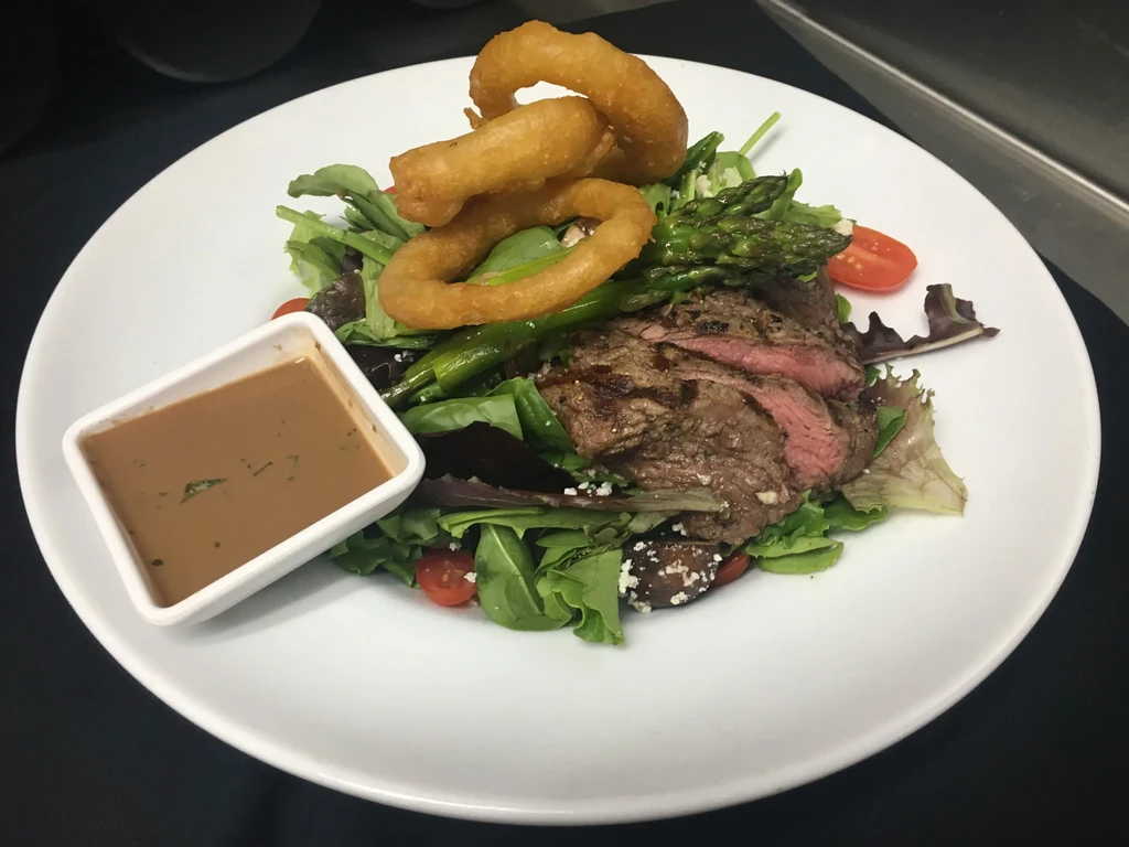 Gourmet steak salad with asparagus, tomatoes, cheese, and onion rings.