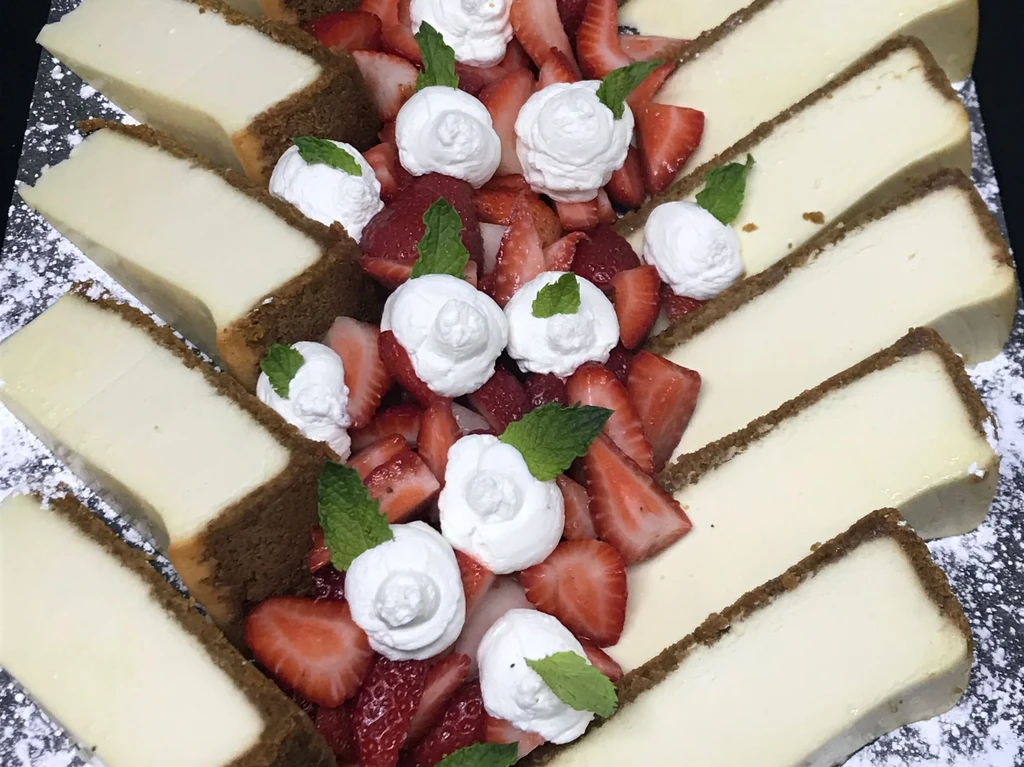 Fanned cheesecake slices, fresh strawberries, whipped cream, and mint garnish.