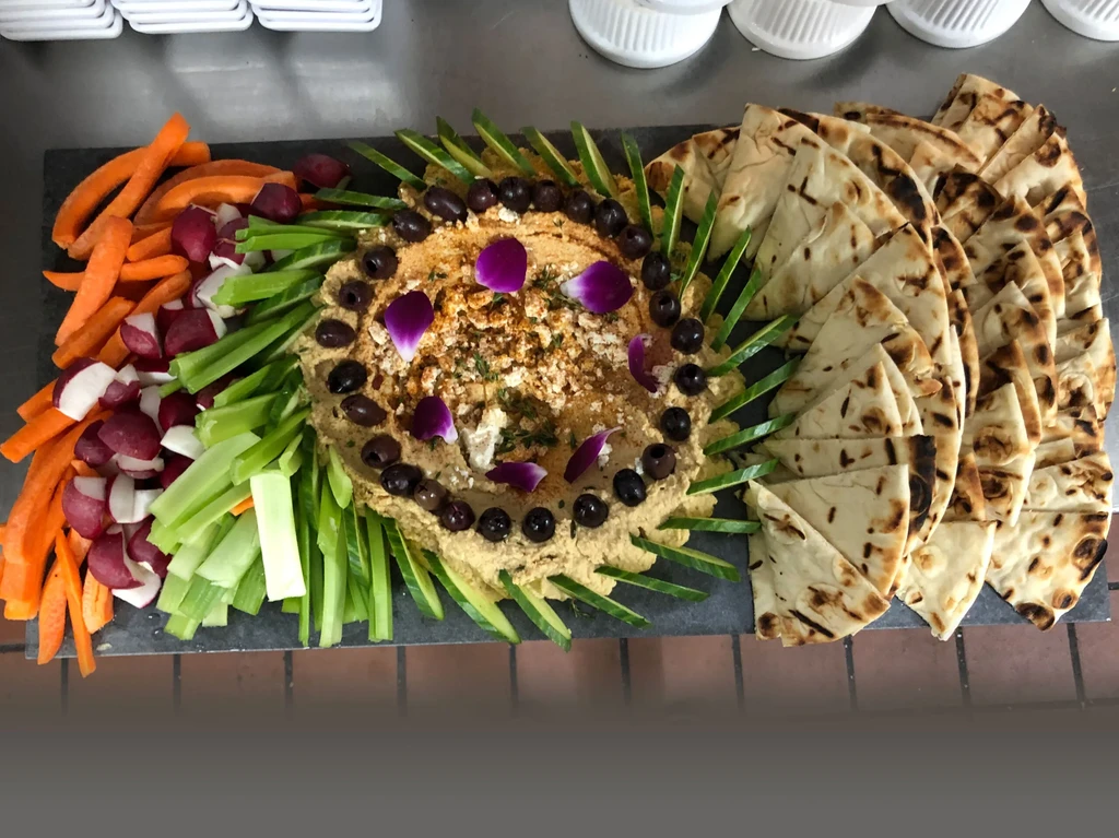 Overhead platter of garnished hummus, crudités, and grilled pita on dark slate.