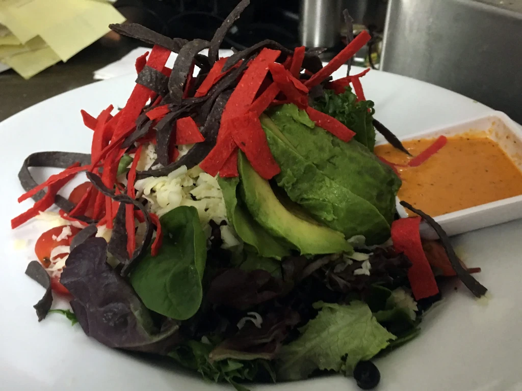 Salad with lettuce, avocado, cheese, tomatoes, tortilla strips, and dressing.