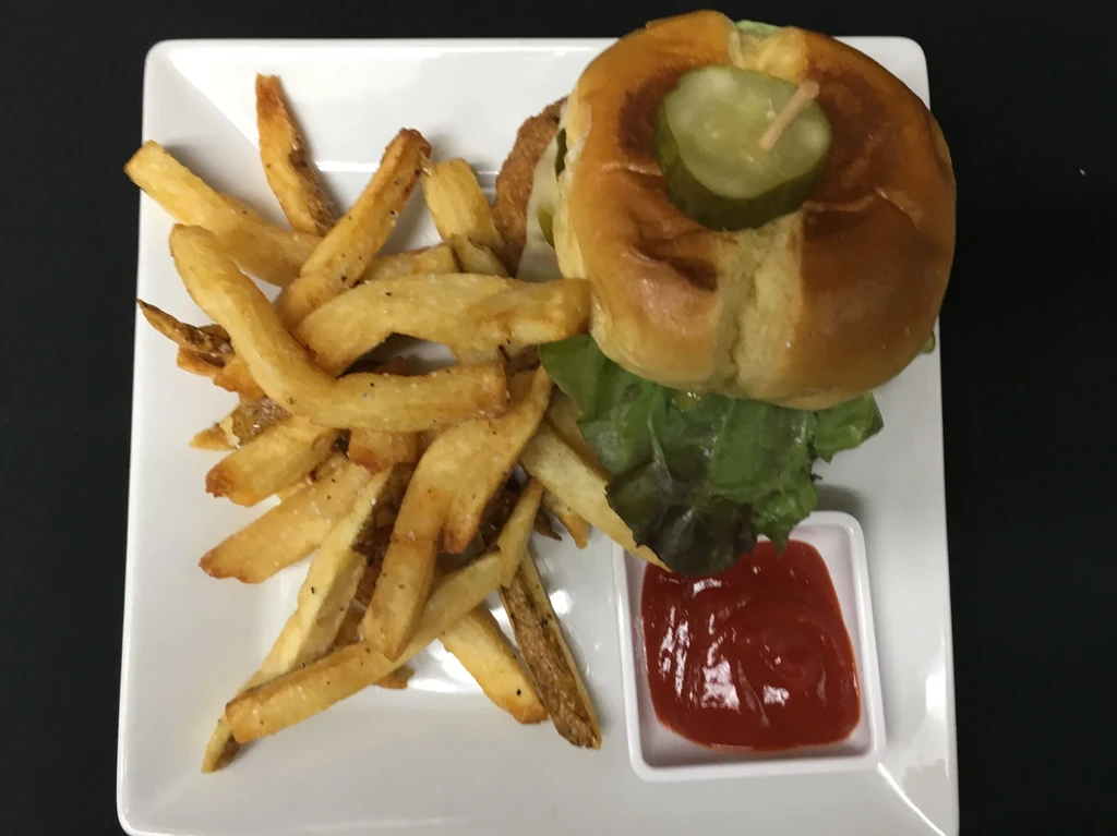 Burger, golden fries, pickle, and ketchup on a white plate.