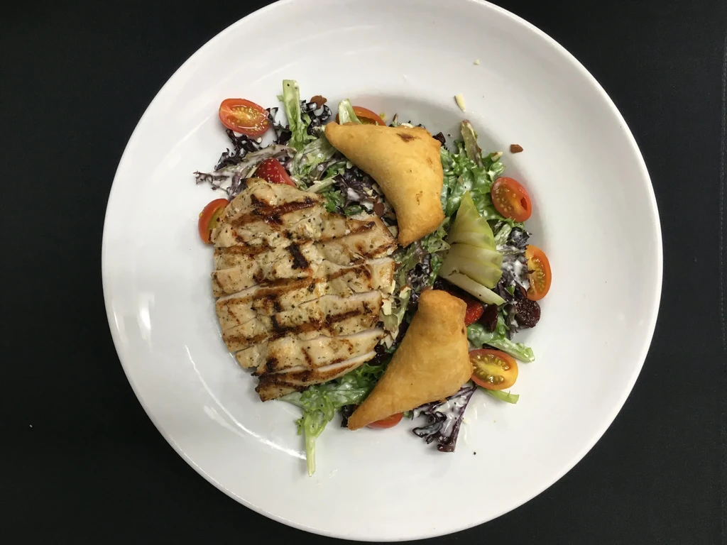 Sliced grilled chicken, mixed salad, and two fried pastries on a plate.