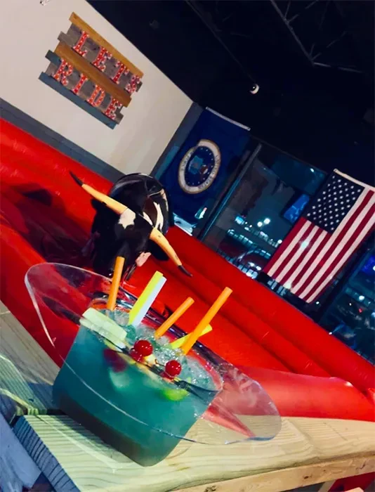 Large blue-green cocktail with fruit; mechanical bull and flags.