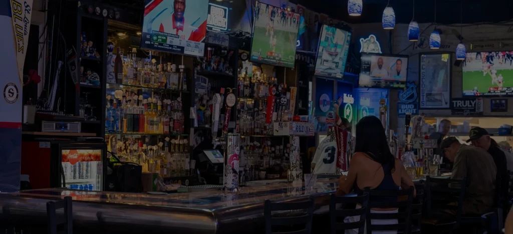 Bustling sports bar interior with a stocked bar, TVs, and patrons.