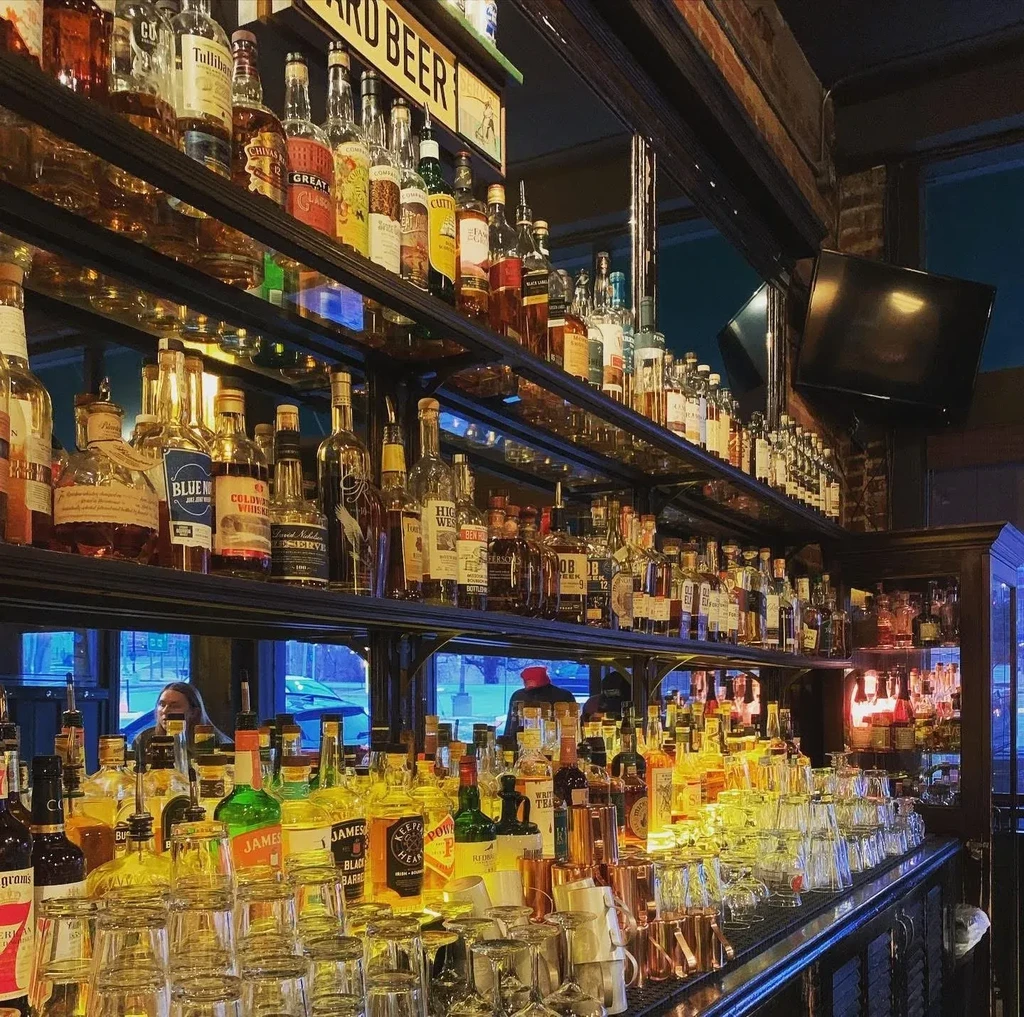 Well-stocked bar shelves filled with diverse liquor bottles and inverted glassware.