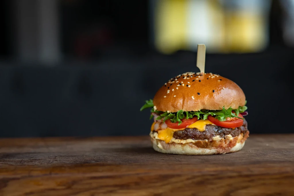 Gourmet beef burger with melted cheese and fresh vegetables on wood.