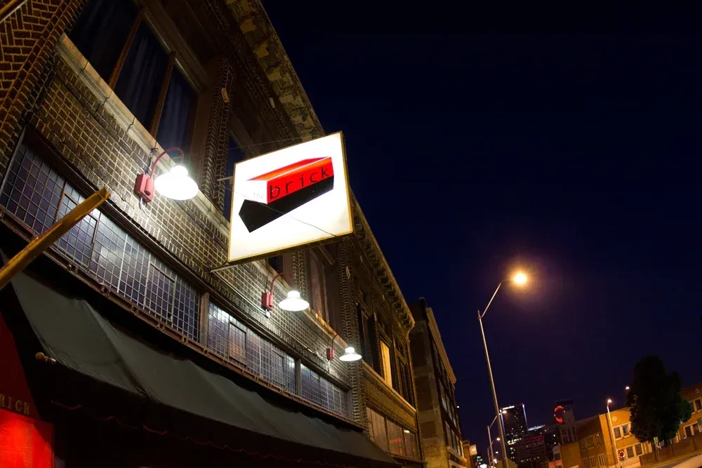 Square 'the brick' sign illuminates a dark brick building at night.
