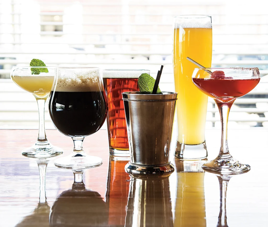 Six different cocktails and beers on a reflective wooden surface.