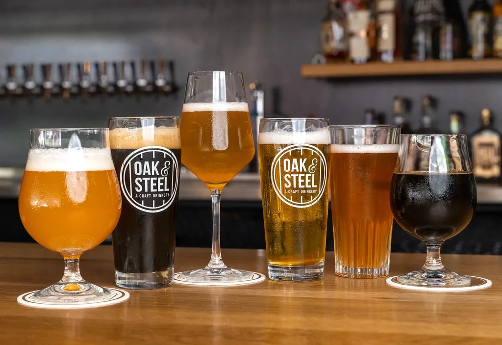 Five distinct craft beverages with logos on a wooden bar.