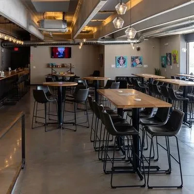 Modern industrial restaurant interior with bar, tables, and colorful art.