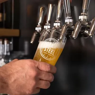 Hands pouring golden beer from a tap into Strong Steel glass.