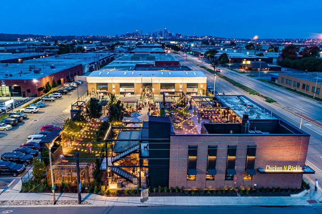 Aerial view of illuminated Chicken N Pickle restaurant complex at dusk.