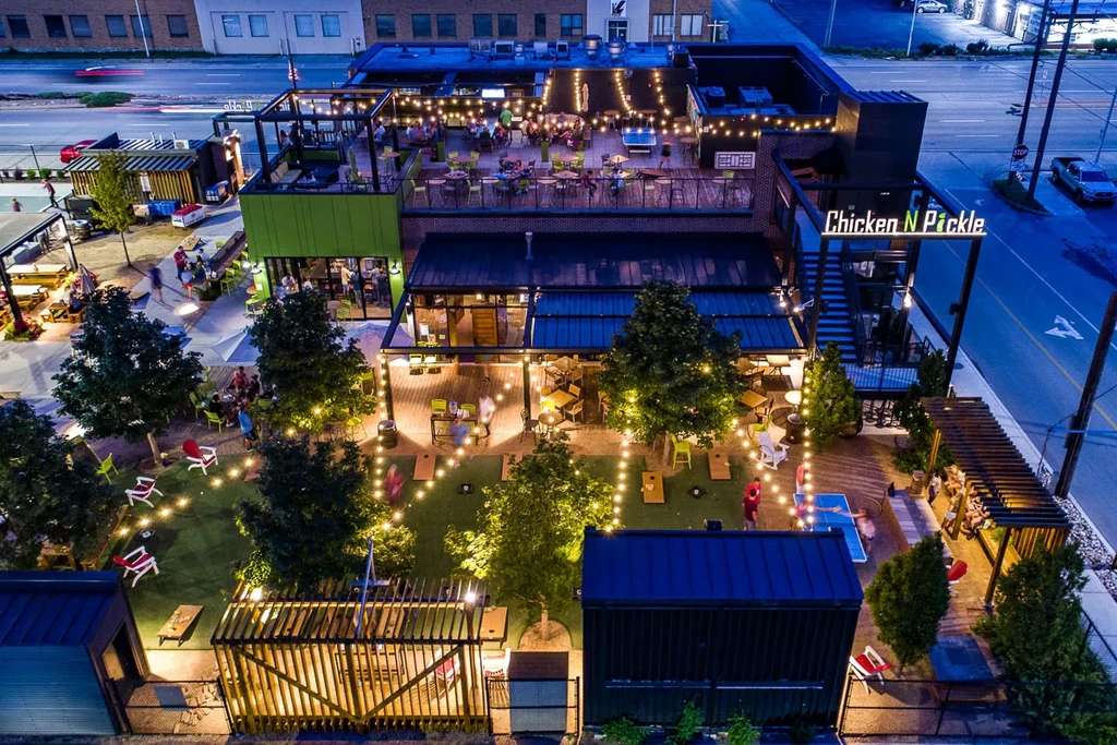 "Chicken N Pickle" multi-level outdoor restaurant complex, illuminated at night.
