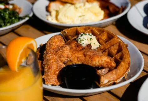 Crispy fried chicken, waffle with butter, and orange juice close-up.