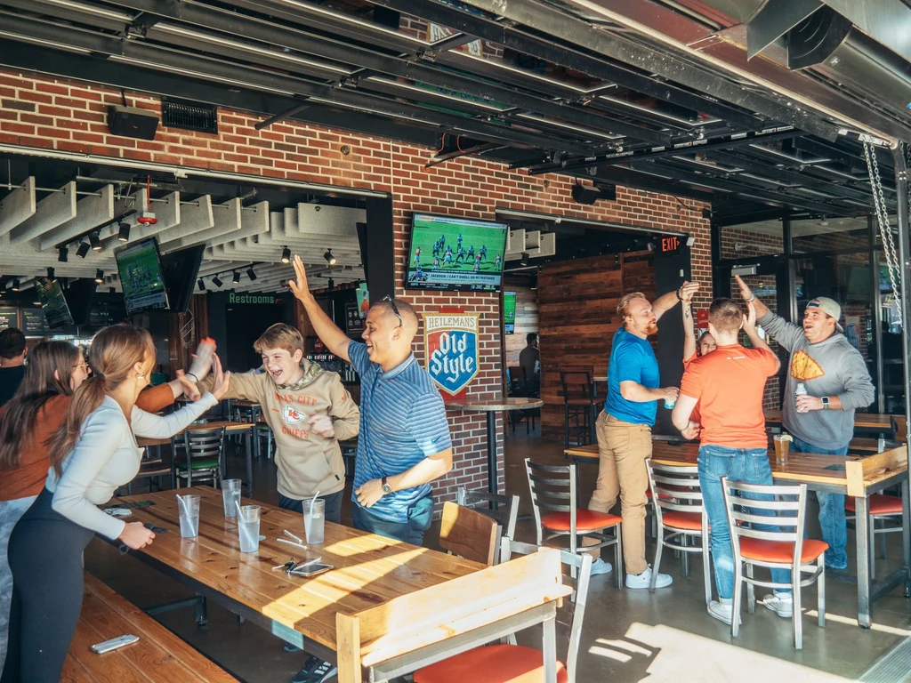 Patrons high-fiving and cheering in a modern, lively sports bar.