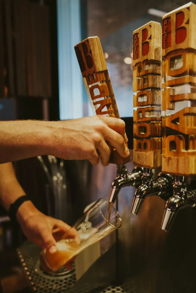 Bartender's hands pouring light beer from a tap with "BORDER" handles.
