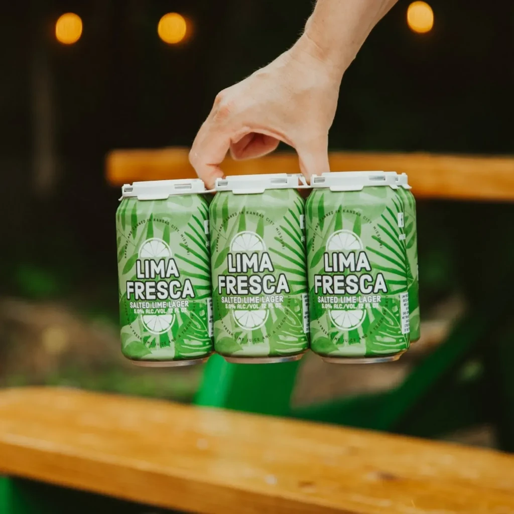 A hand holds three green Lima Fresca Salted Lime Lager cans.