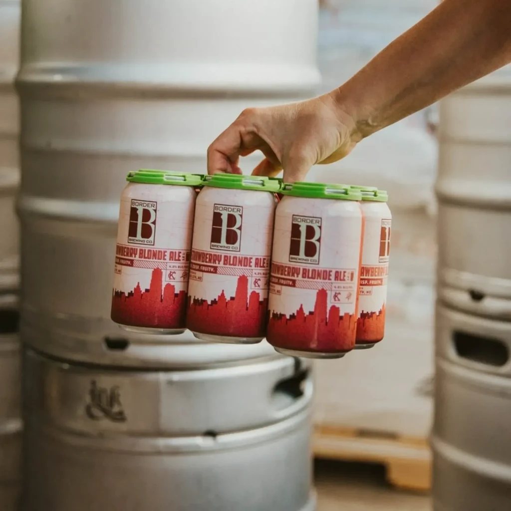 Hand holding a Border Brewing Co. Strawberry Blonde Ale 4-pack.