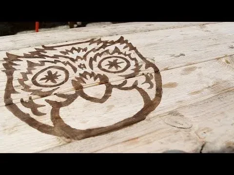 Close-up of abstract dark owl design on rustic wood planks.