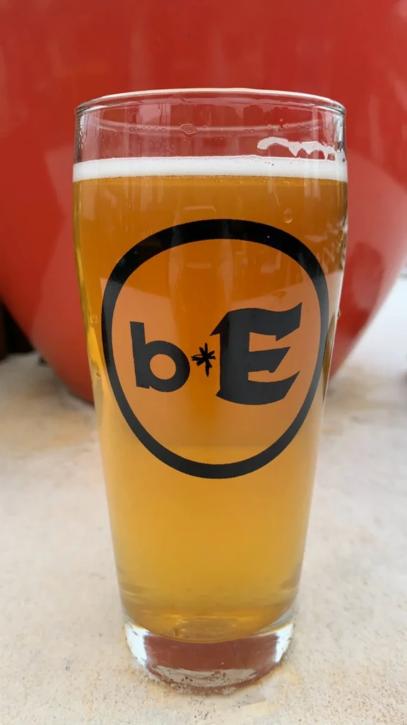 Clear pint of beer with 'b * E' logo, red background.