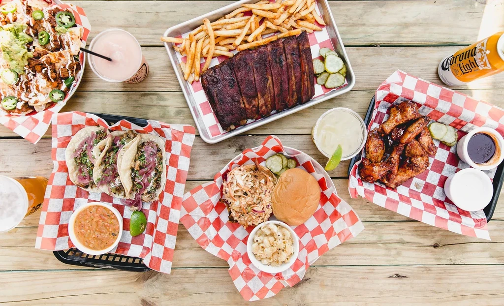 Overhead of a rustic table with nachos, ribs, tacos, wings, and drinks.