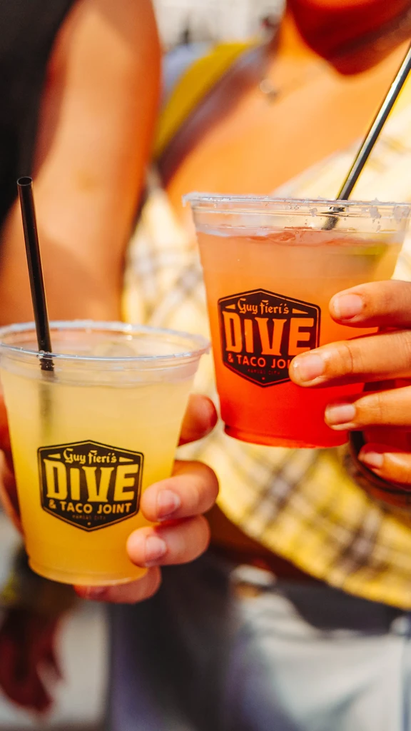 Two plastic cups with yellow and orange Guy Fieri drinks.