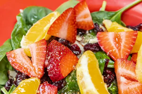 Vibrant salad of strawberries, orange, dried berries, spinach on red plate.