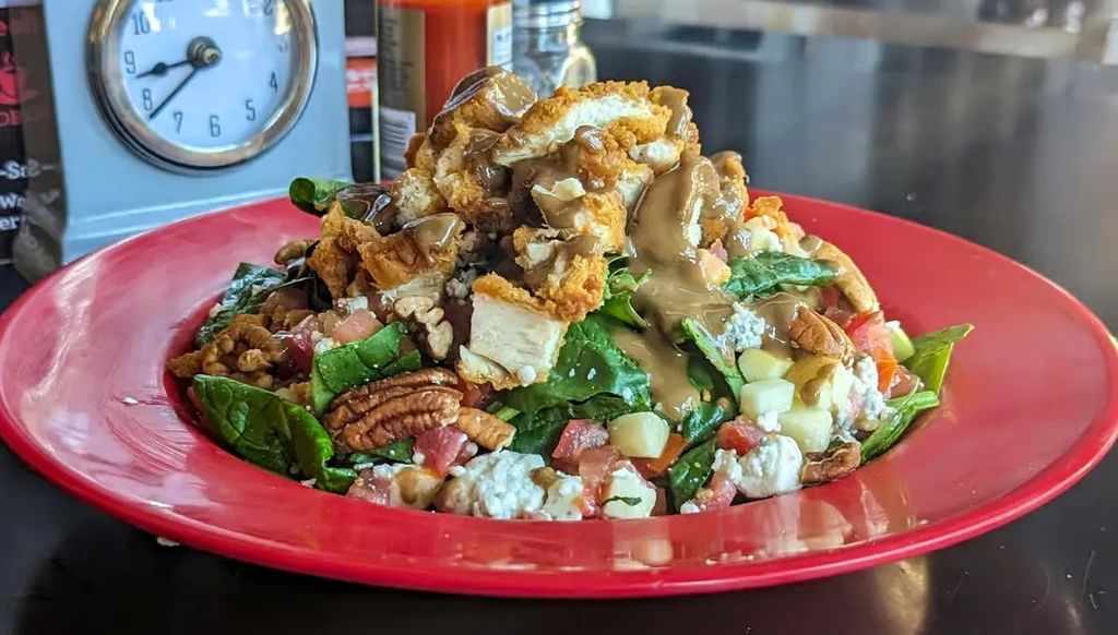 Crispy fried chicken salad with spinach, cheese, and pecans on red plate.