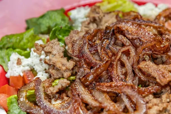 Close-up: Gyro meat, crispy onions, fresh salad, and feta in red dish.