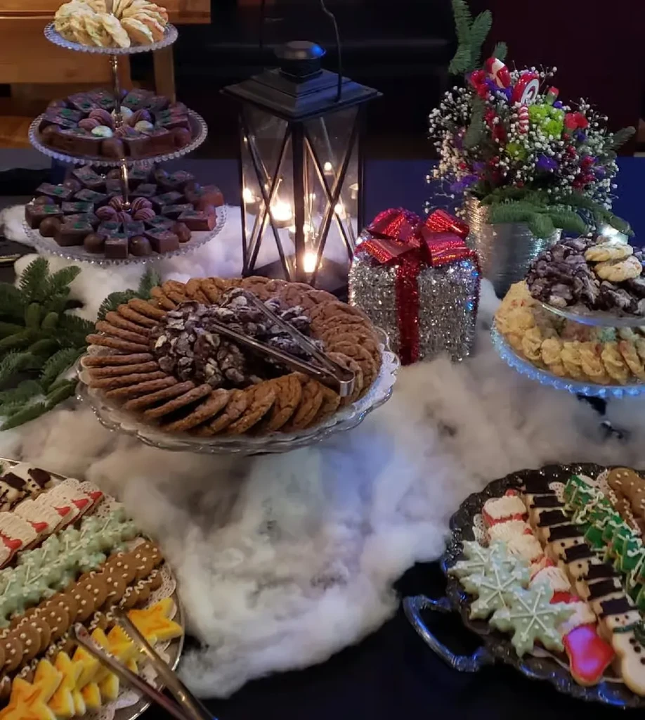 Festive dessert table with cookies, chocolates, lantern, and snowy decorations.