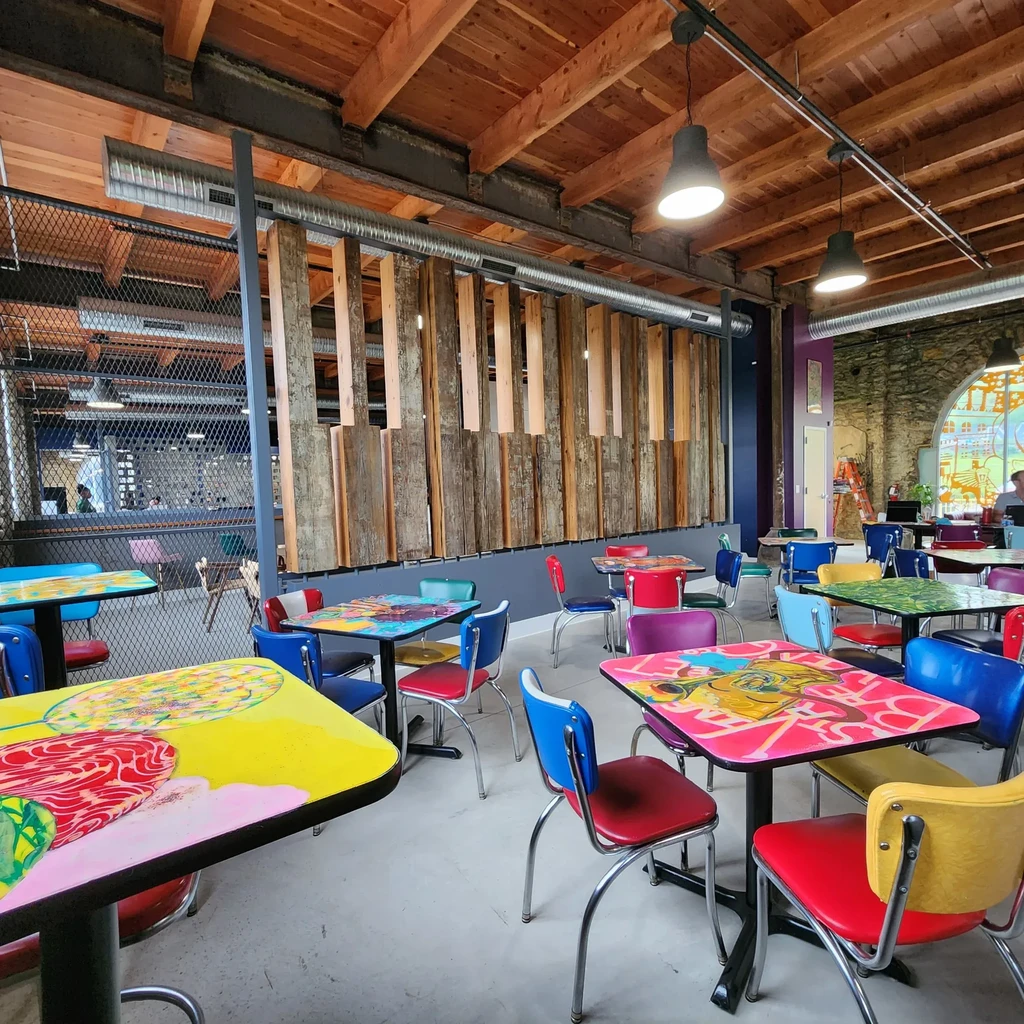 Vibrant restaurant interior with pop-art tables, bright chairs, and exposed beams.