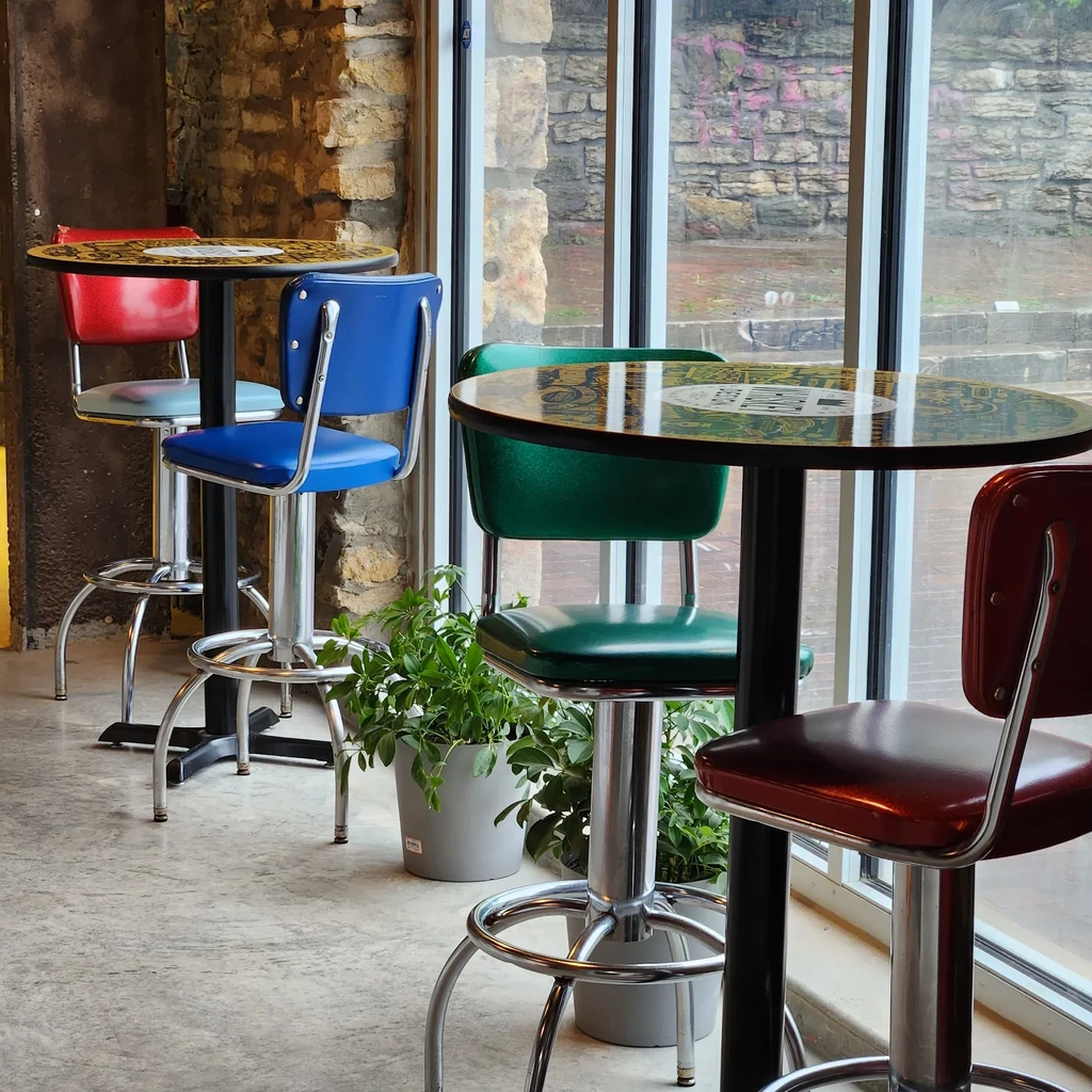 Retro diner high-top tables with red, blue, green stools by window.