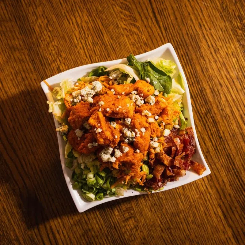 Overhead Buffalo chicken salad with blue cheese, bacon, and greens.