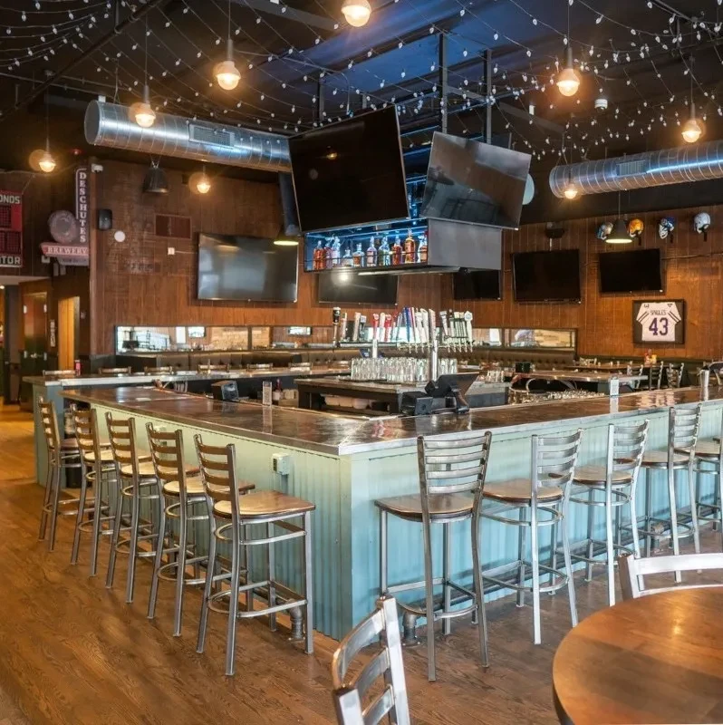 Modern sports bar interior with L-shaped bar, numerous TVs, and wood decor.