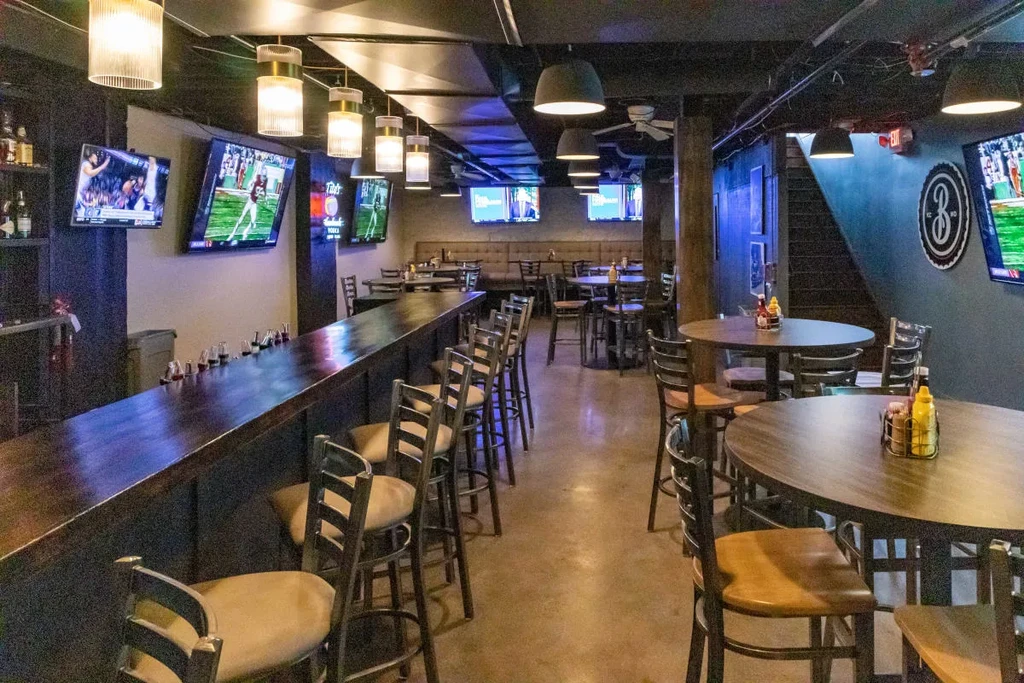 Empty sports bar interior with dark wood bar and multiple sports TVs.