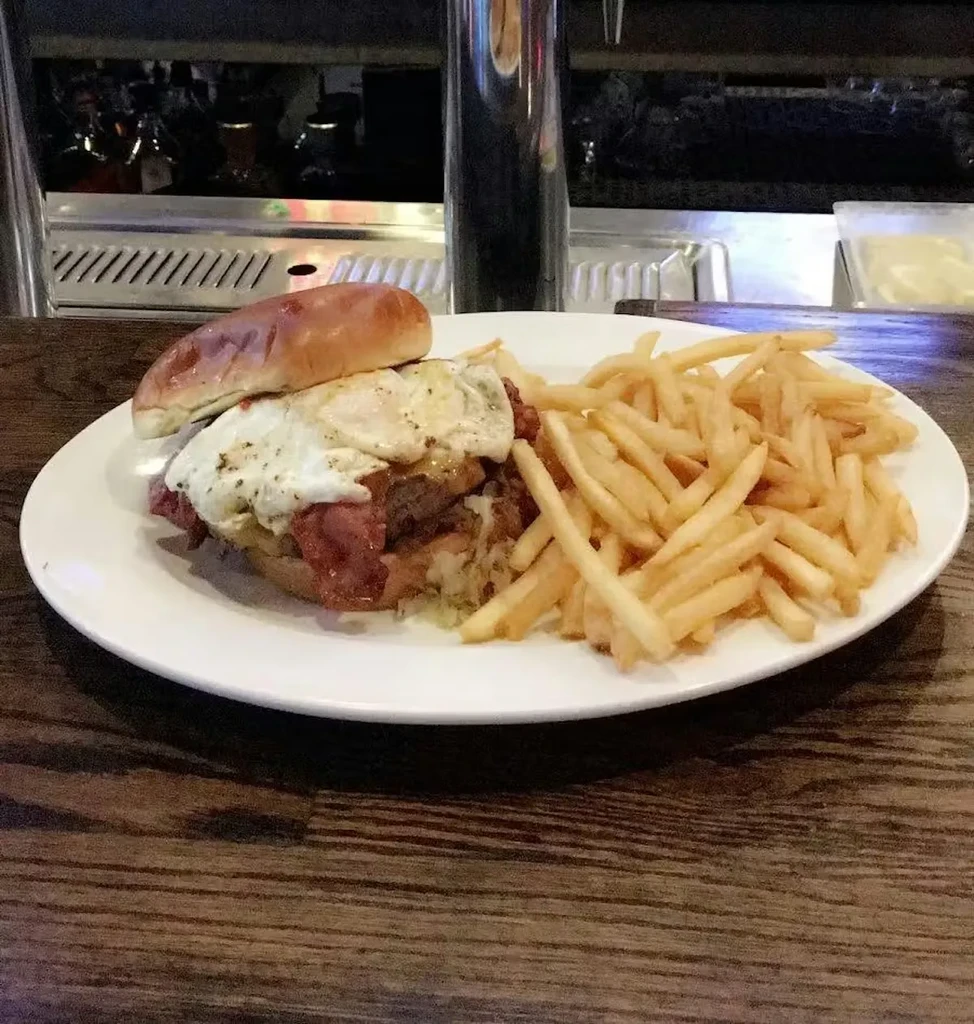 Hearty burger with fried egg, bacon, and fries on a rustic table.