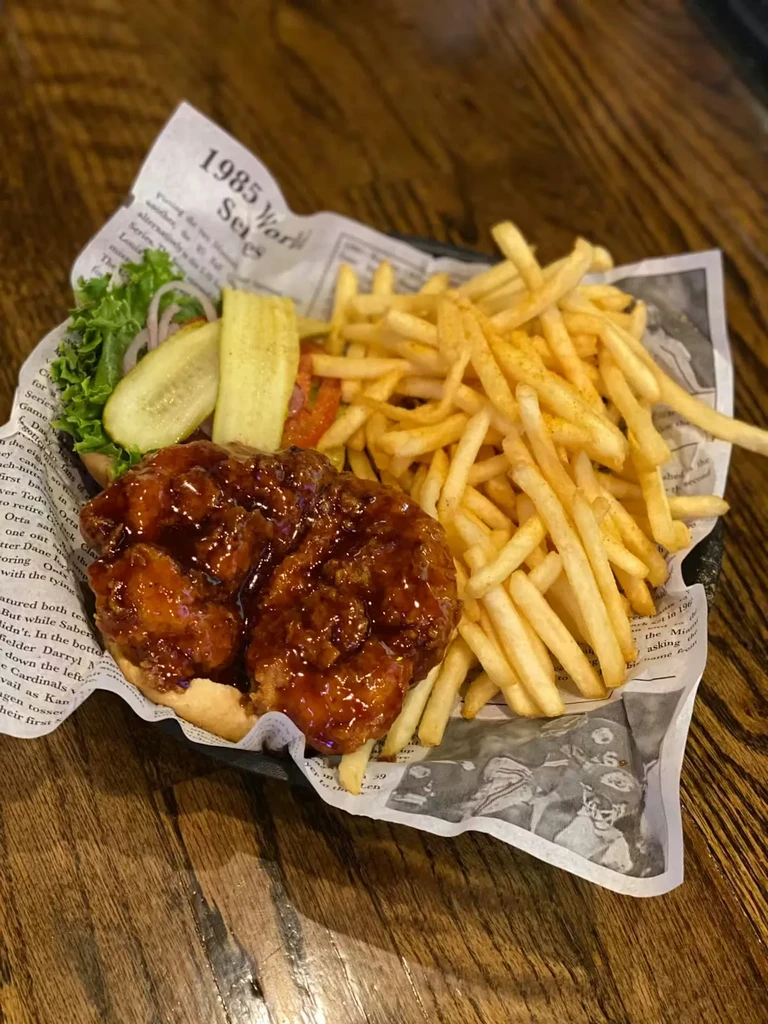 Overhead view of dark-sauced fried chicken sandwich, fries, and pickles.