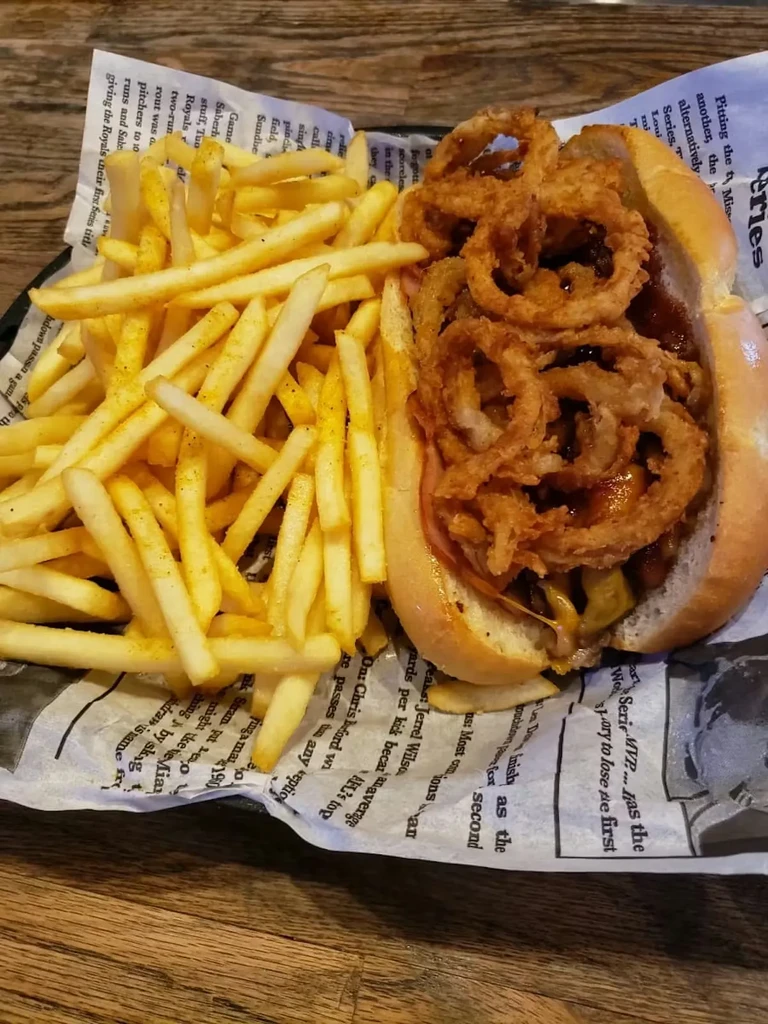Hot dog, onion rings, and fries in a basket on wood.