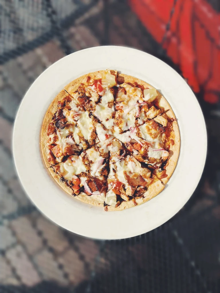 Top-down chicken, pineapple, tomato, cheese, onion pizza with dark sauce.