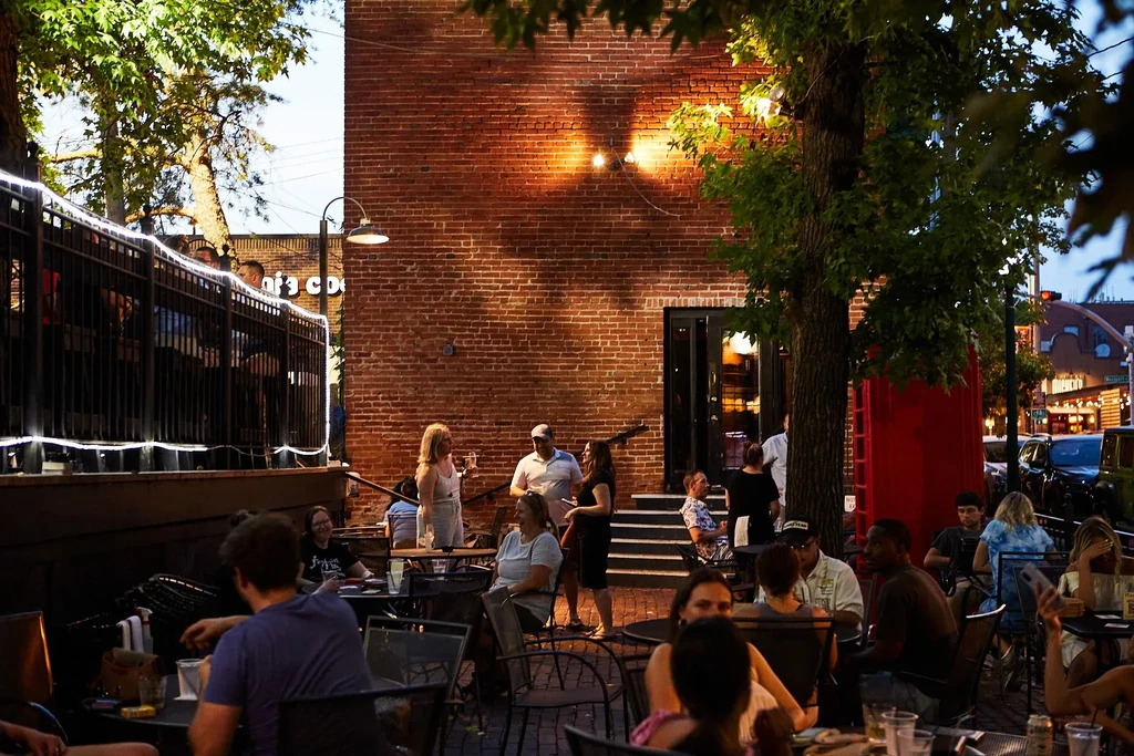Outdoor restaurant patio with people and warm string lights.