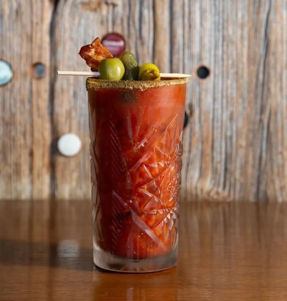 Bloody Mary in faceted glass with olives, pickles, and fried chicken.