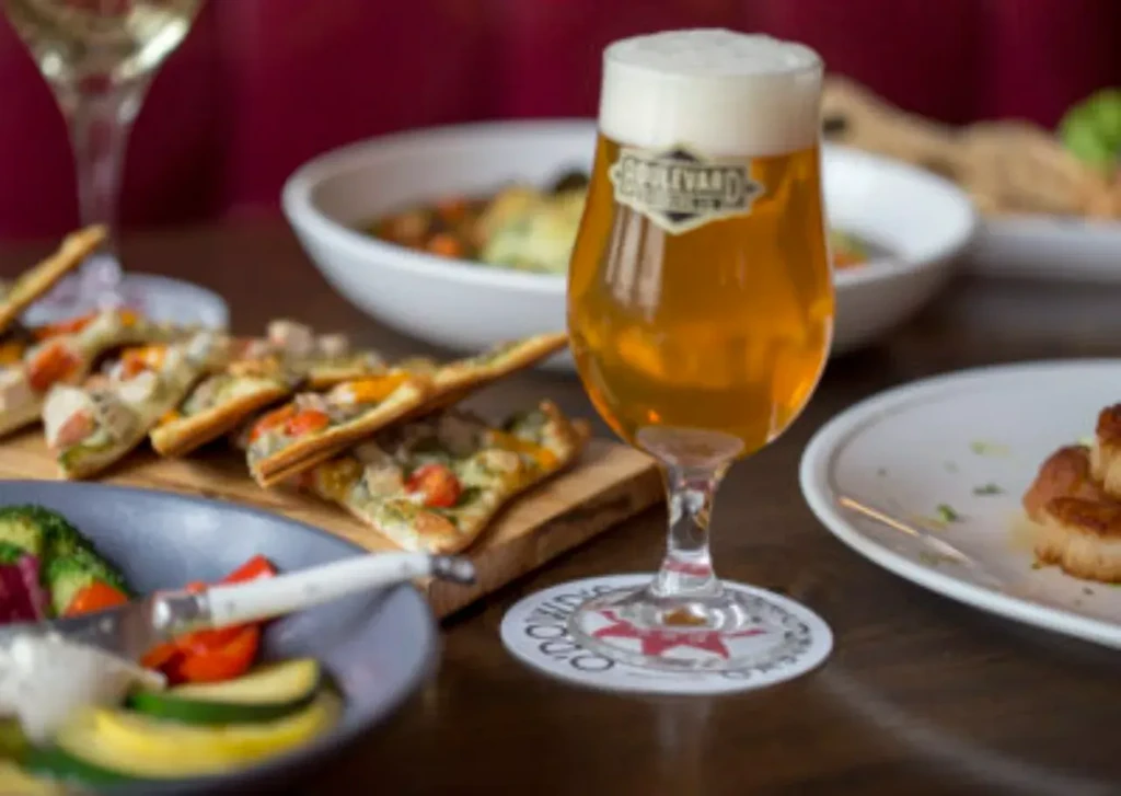 Boulevard beer, pesto flatbread, vegetables, and scallops on a restaurant table.