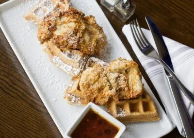 Crispy fried chicken and waffles with powdered sugar and dipping sauce.
