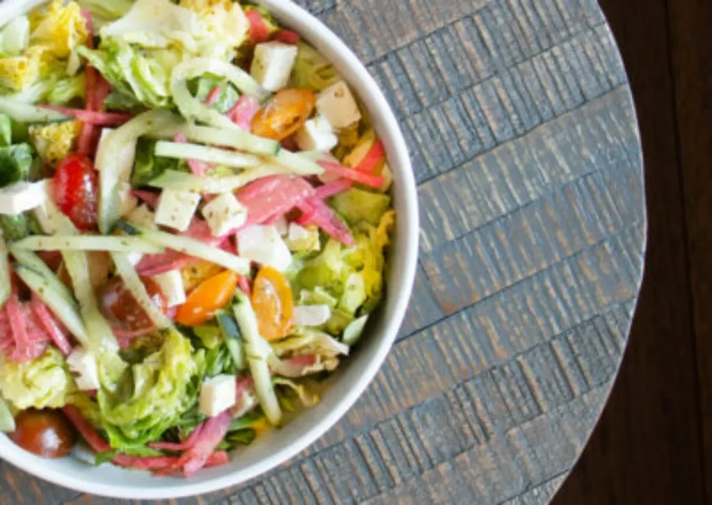 Mixed green salad with tomatoes, cucumber, and white cheese on wood.