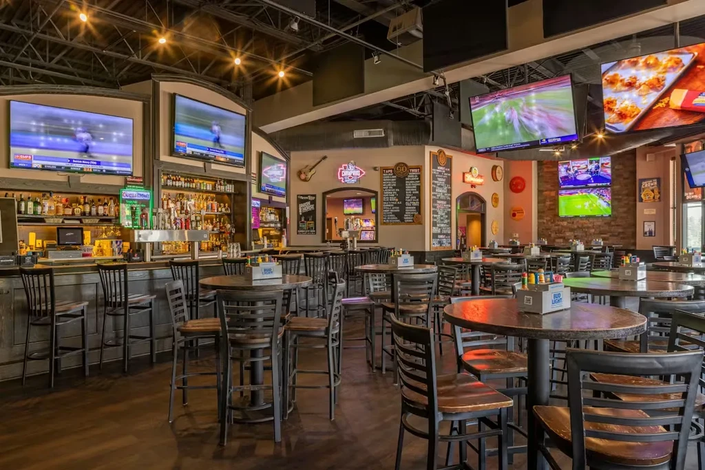 Empty modern sports bar with stocked bar, high tables, and sports TVs.