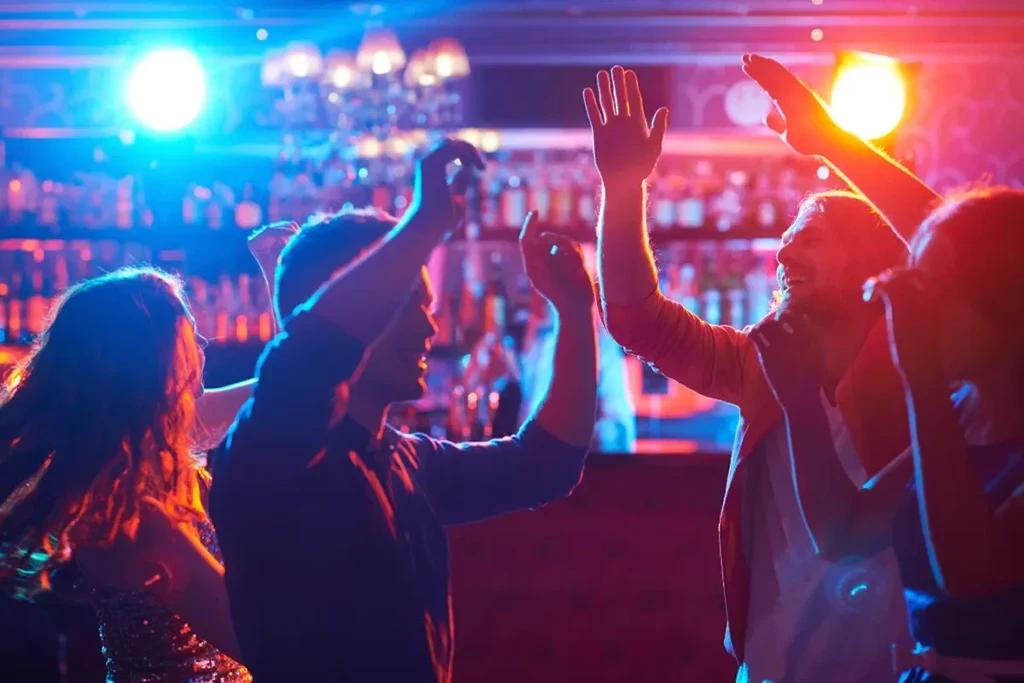Silhouetted people dancing under bright blue and red club lights.