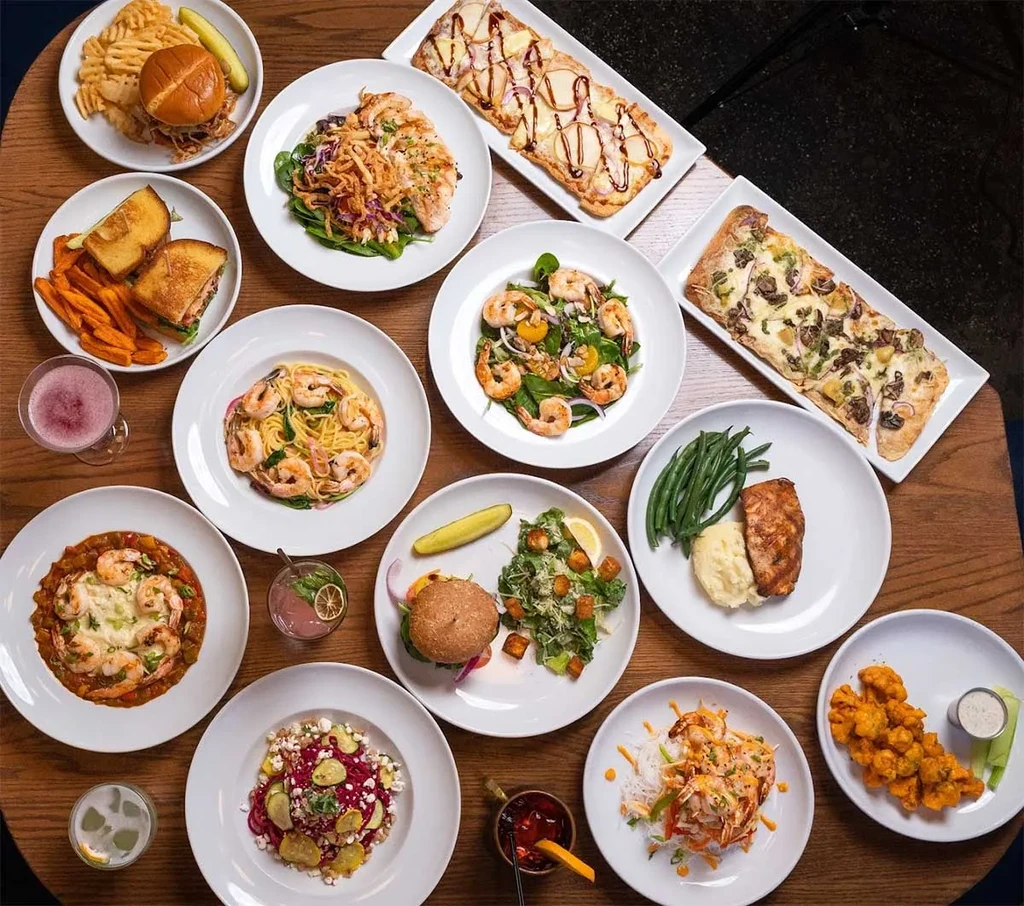 Overhead view of many diverse dishes and drinks on a wooden table.